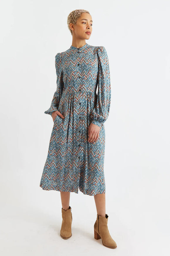 Create an artful look with this stylish Louche London NAYMA Duck-Egg Art Print Midi Dress. Crafted in a teal geometric chevron print with accents of camel and red. This button through midi-length dress features an elegant banded neckline, long billowing sleeves, and side pockets.